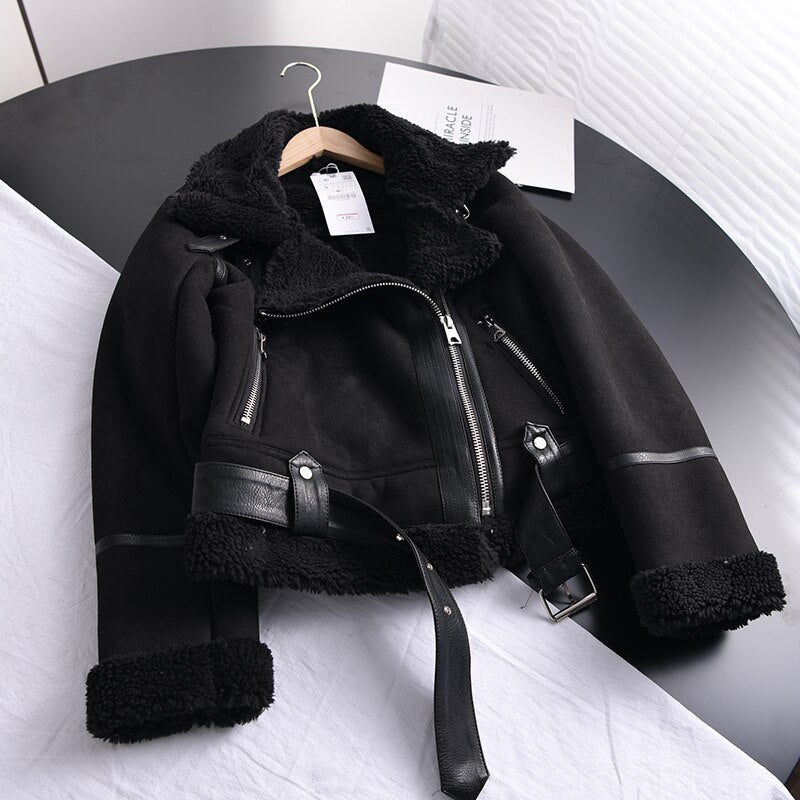 Schwarze Bikerjacke aus Leder mit Fellfutter, Reißverschluss und Gürtel auf Tisch.