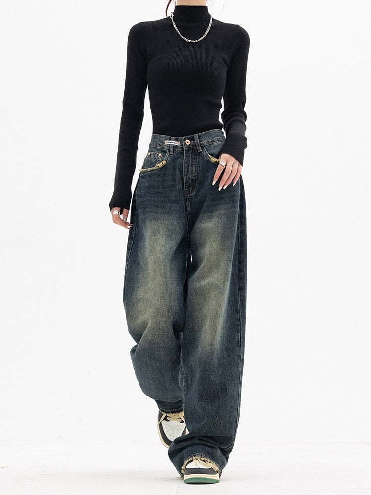 Frau in schwarzem Pullover und weiten Jeans, Streetwear-Mode, lässiger Stil, weiße Sneakers.
