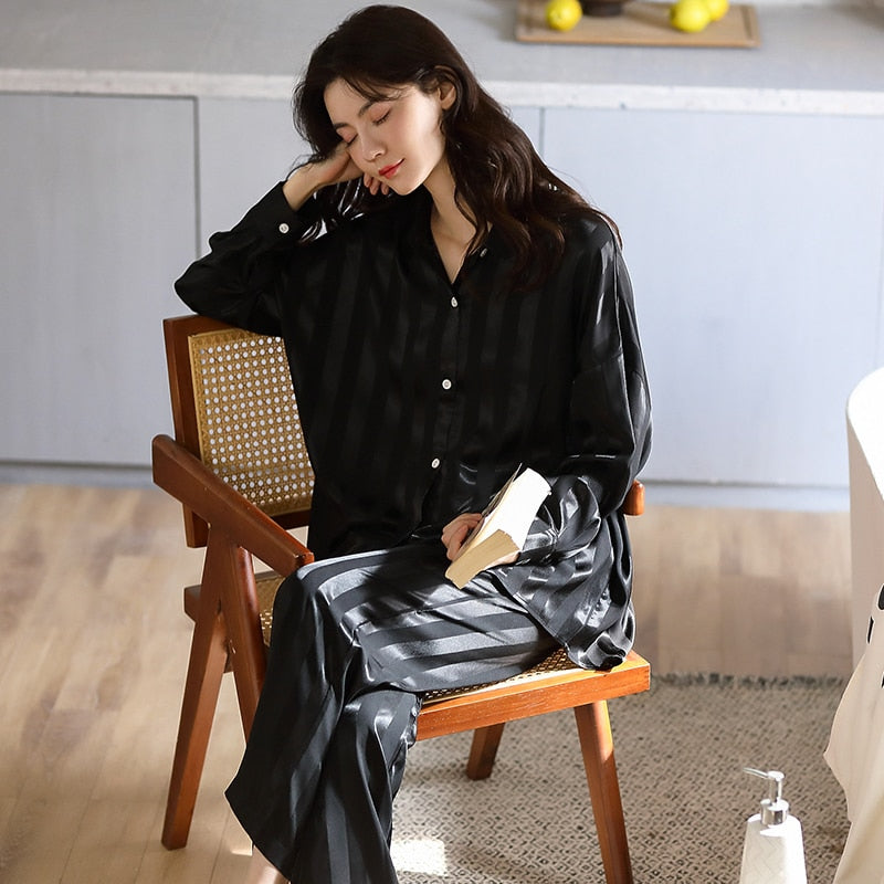 Frau in schwarzem Satin-Pyjama sitzt auf Holzstuhl, gemütliche Nachtwäsche, modernes Design.