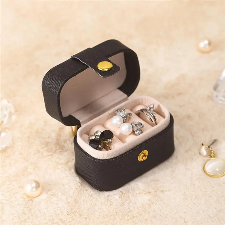 Schwarze Schmuckbox aus Leder mit Ringen und Perlen, kompakt, ideal für Reisen.