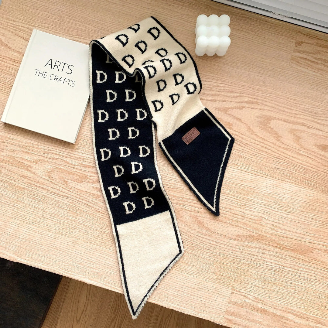 Schwarzer und beiger Designer-Schal mit D-Muster auf Holztisch neben Buch und Kerze.