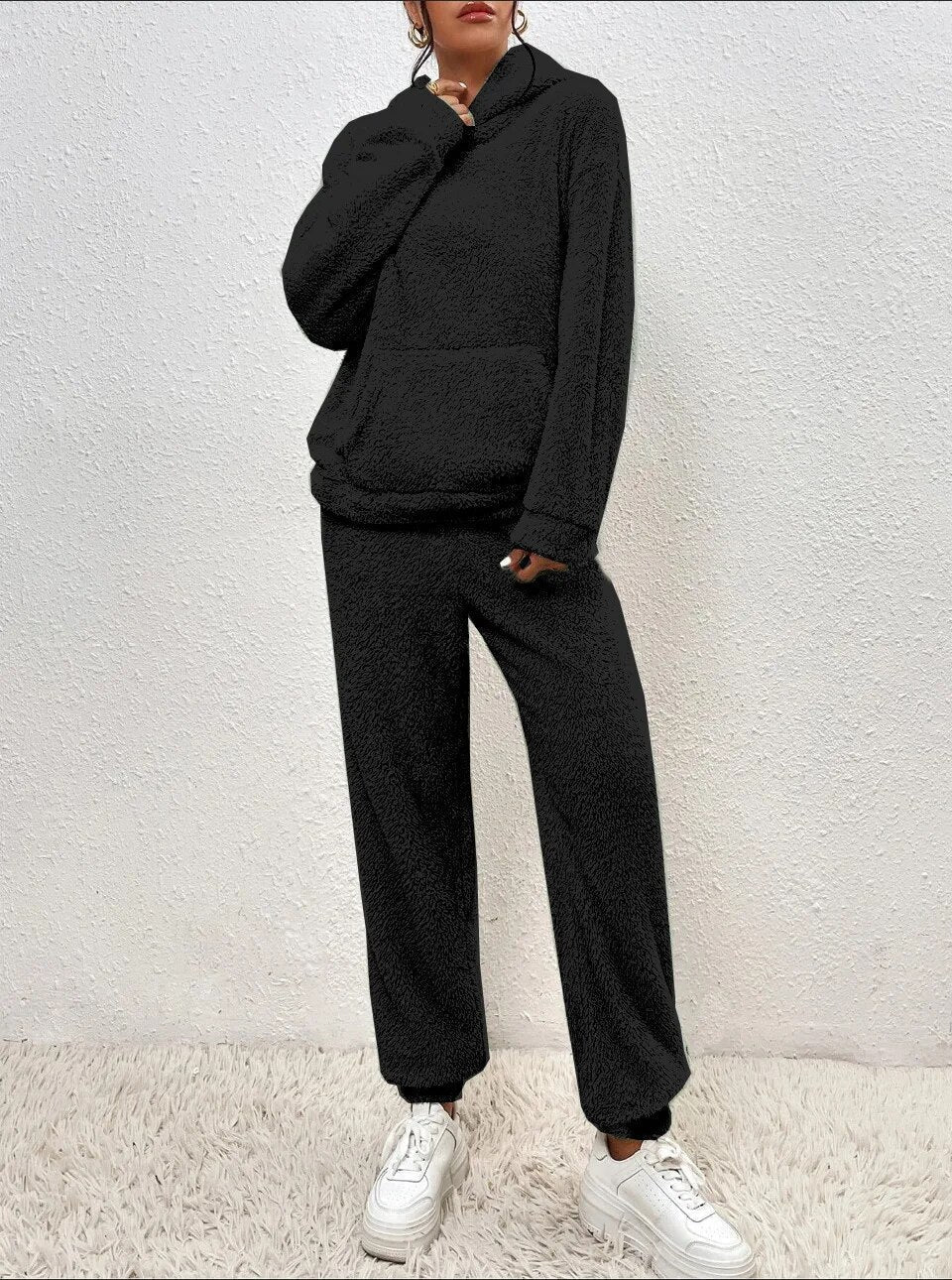 Frau in schwarzem Fleece-Hoodie und Jogginghose, weiße Sneaker, gemütliche Wintermode.