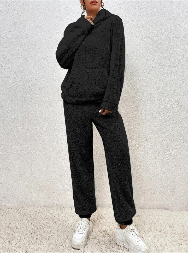 Frau in schwarzem Fleece-Hoodie und Jogginghose, weiße Sneaker, gemütliche Wintermode.
