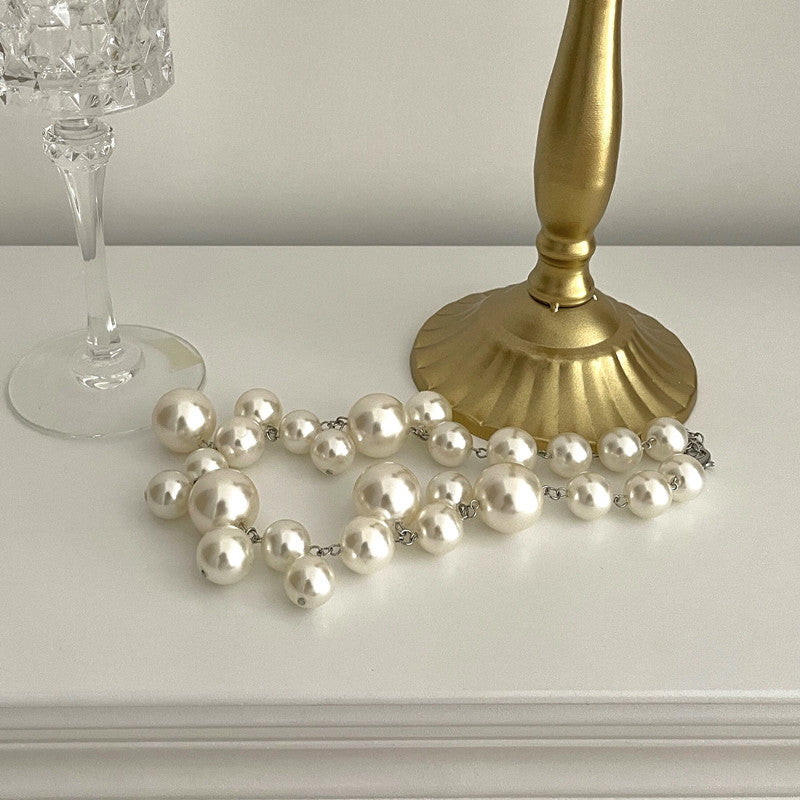 Perlenkette auf weißem Tisch neben goldener Lampe und Kristallglas.