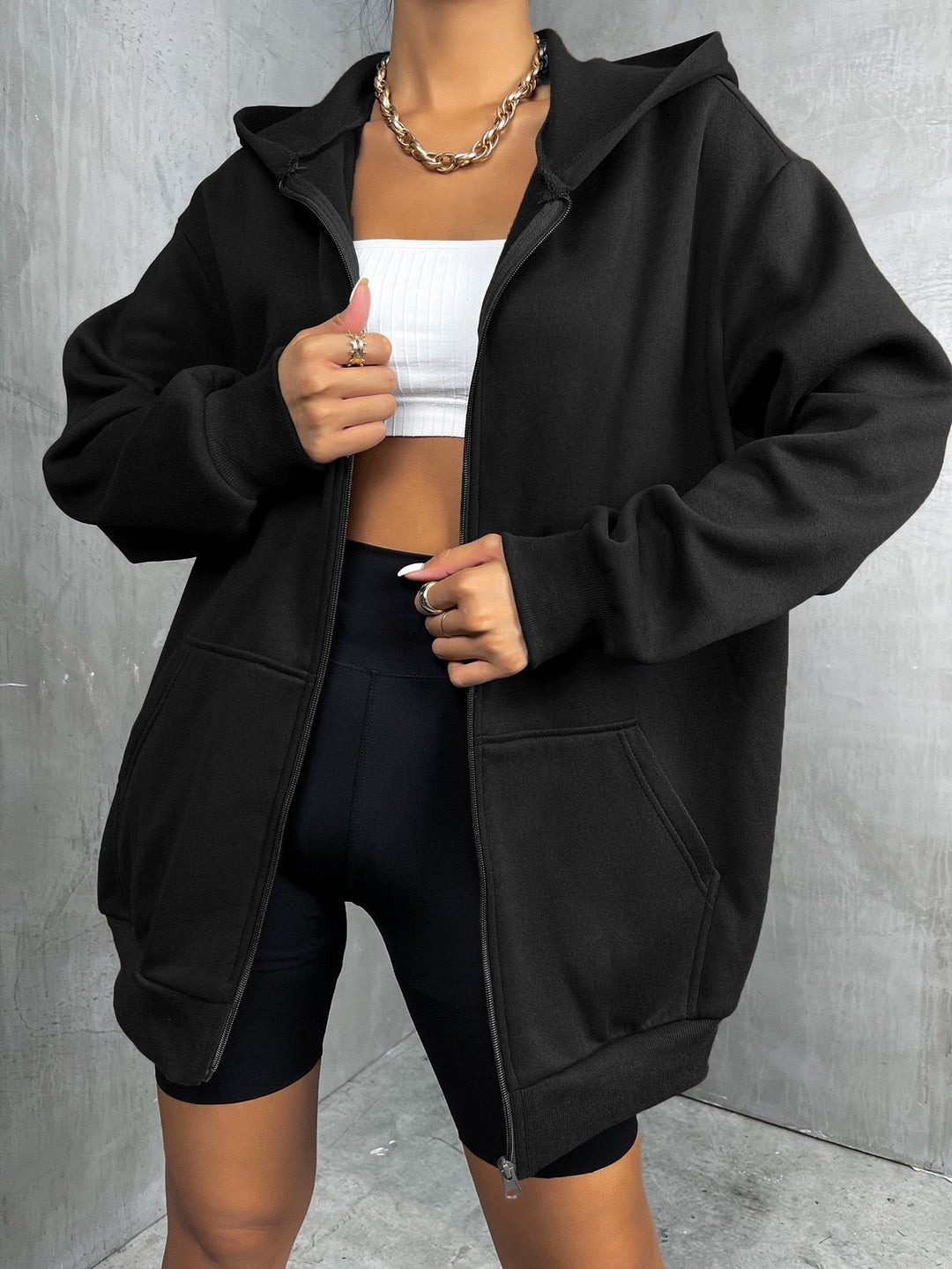 Frau in schwarzem Oversize-Hoodie, weißem Top und Radlerhose, modisch, lässig, urbaner Stil.