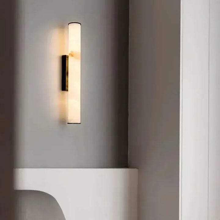 Svítidlo s tmavým držákem na šedé stěně nad bílým zaobleným nábytkem, vedle světlého sloupku. 20