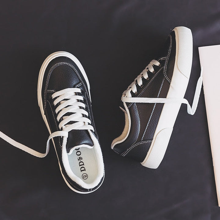Schwarze Leder-Sneaker mit weißen Schnürsenkeln auf dunklem Hintergrund, modisch und bequem.