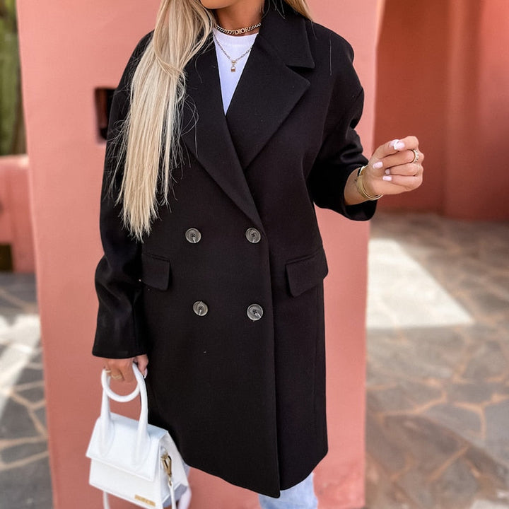 Frau in schwarzem Wollmantel mit weißen Knöpfen, hält weiße Handtasche, modisch, elegant.