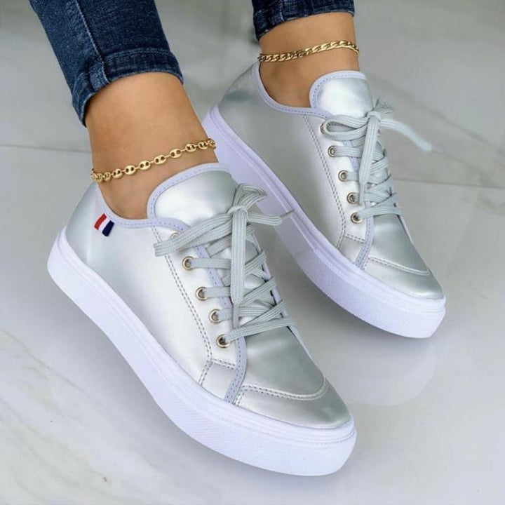 Silberne Damen-Sneaker mit weißer Sohle, Schnürsenkeln und goldener Fußkette.