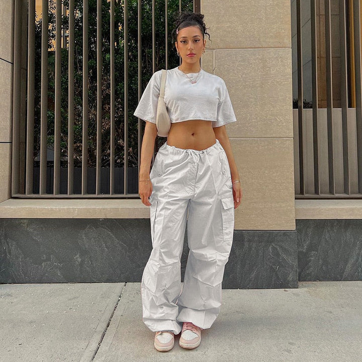 Frau in weißem Crop-Top und Cargo-Hose, urbaner Stil, Sommermode, Streetwear, Sneakers.
