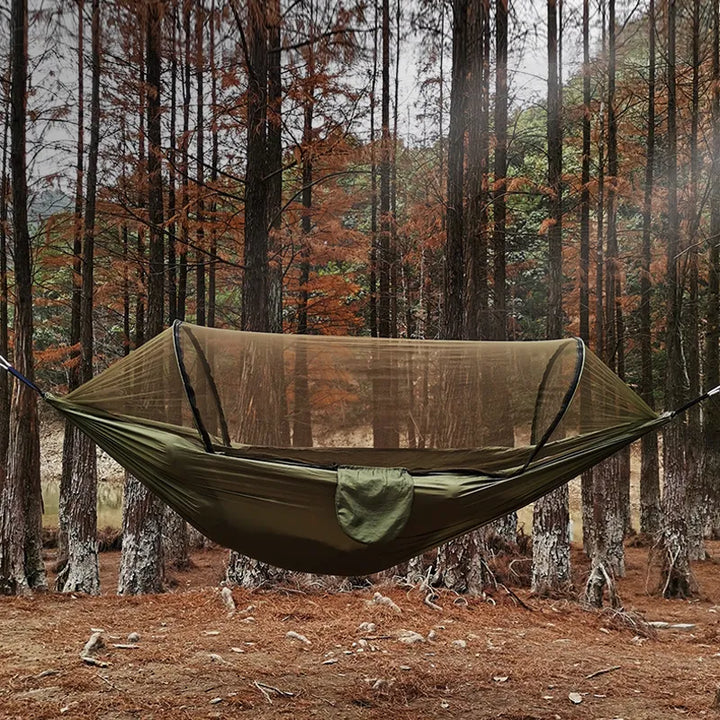 Grüne Hängematte mit Moskitonetz im Wald, Campingausrüstung, Outdoor-Abenteuer, Herbstlaub.