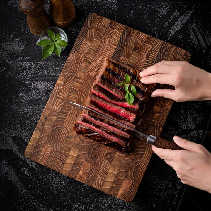 Hände schneiden gegrilltes Steak auf Holzbrett, schwarzer Hintergrund, Gewürze, Basilikum.