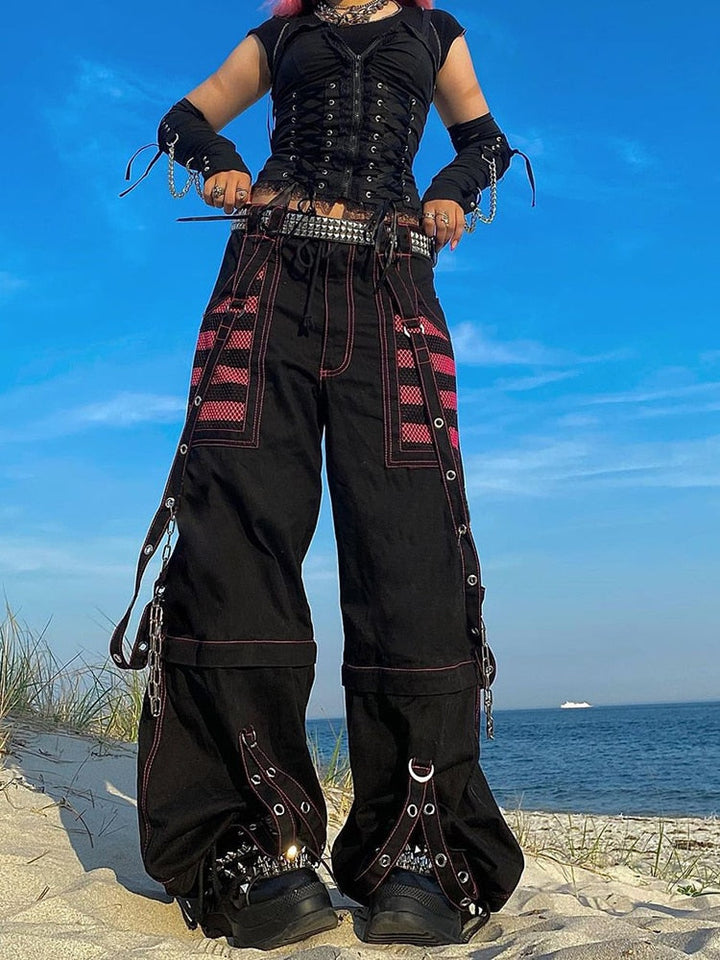 Frau in schwarzer Gothic-Hose mit pinken Streifen am Strand, alternative Mode, Sommer.