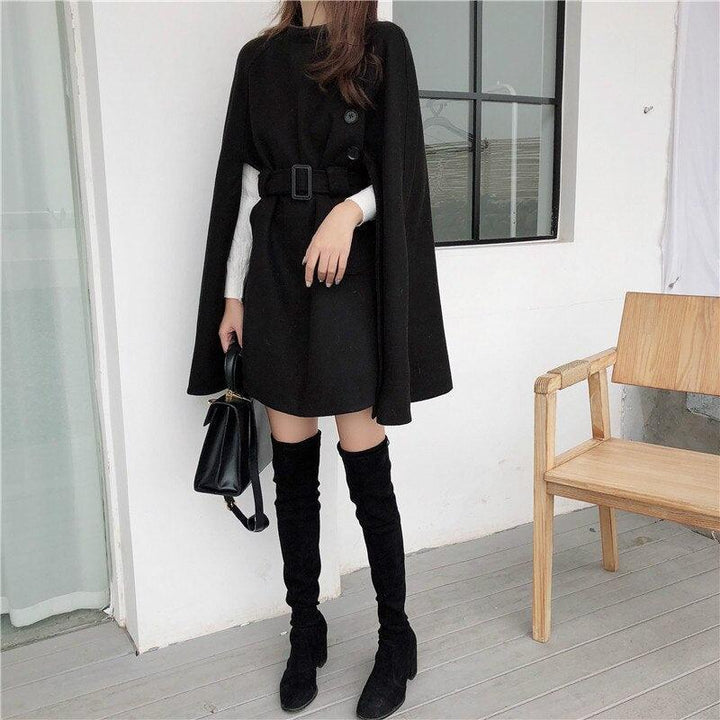 Frau in schwarzem Cape-Kleid mit Gürtel, Overknee-Stiefeln, Handtasche, moderne Mode.