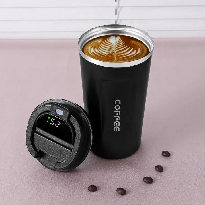 Schwarzer Thermobecher mit Latte Art, digitalem Temperaturdisplay, Kaffeebohnen daneben.