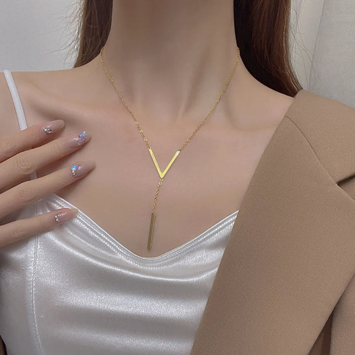 Frau mit goldener V-förmiger Halskette, elegantes Design, weißes Satin-Top, beige Blazer.