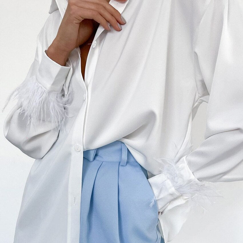 Weiße Bluse mit Federn an den Ärmeln, kombiniert mit hellblauer Hose, elegante Damenmode.