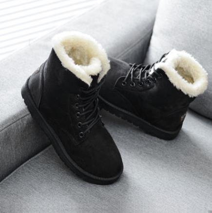 Schwarze Winterstiefel mit weißem Kunstfellfutter auf grauem Sofa, warm und stilvoll.