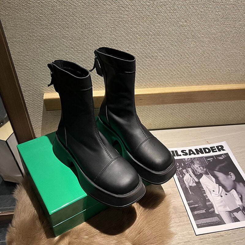 Schwarze Lederstiefel auf grünem Karton, modisch, robust, mit Reißverschluss, Damenmode.