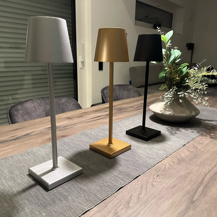 Drei moderne Tischlampen in Silber, Gold und Schwarz auf Holztisch, minimalistisch, LED-Beleuchtung.