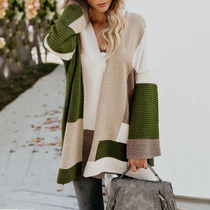 Frau in langem, gestreiftem Strickpullover in Grün, Beige und Weiß mit grauer Handtasche.