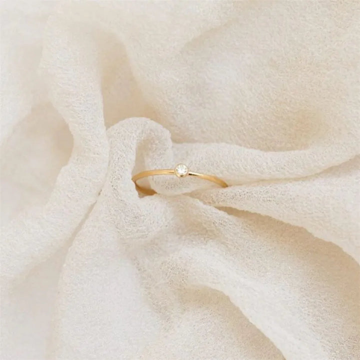 Goldener Ring mit Diamant auf cremefarbenem Stoff, eleganter Schmuck, minimalistisches Design.