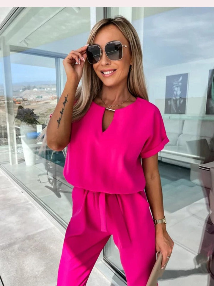 Frau in pinkem Jumpsuit mit Sonnenbrille, lächelnd auf Terrasse, modisch, Sommeroutfit.