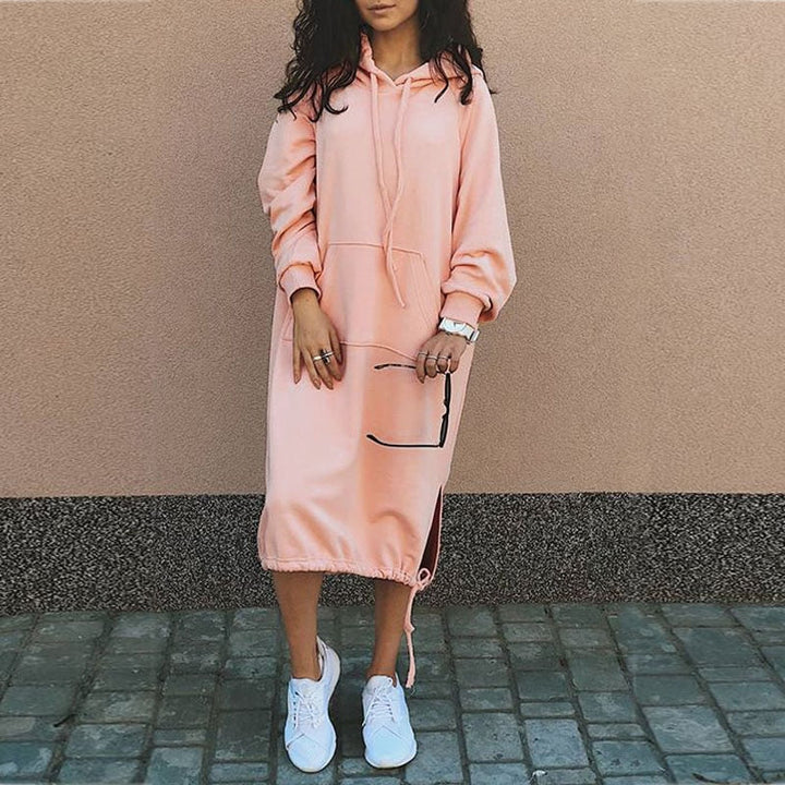 Frau in rosa Kapuzenkleid, lässig, mit weißen Sneakers, modisch, urbaner Stil.