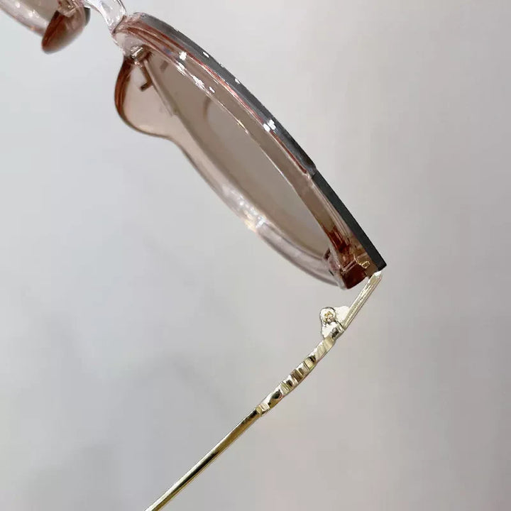Transparente Sonnenbrille mit rosafarbenem Rahmen und goldenen Bügeln, modisches Accessoire.