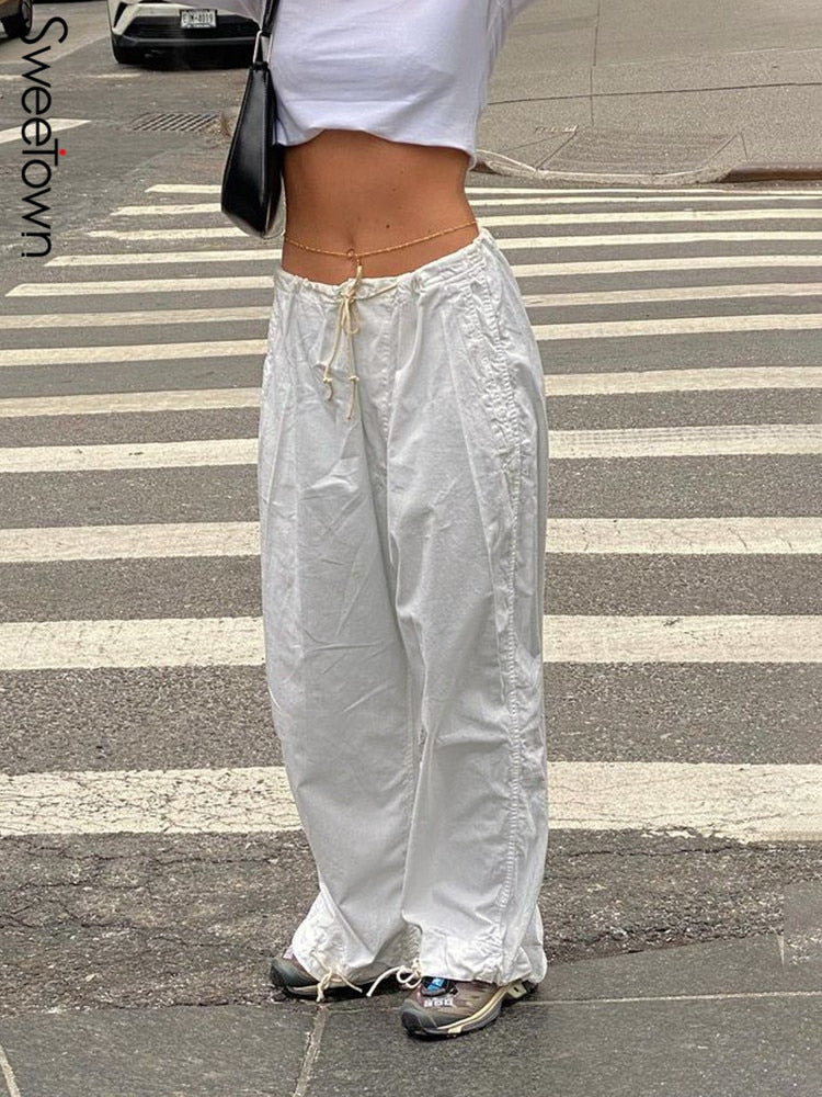 Frau in weißen Baggy-Hosen und Crop-Top auf Zebrastreifen, modisch, urbaner Stil.