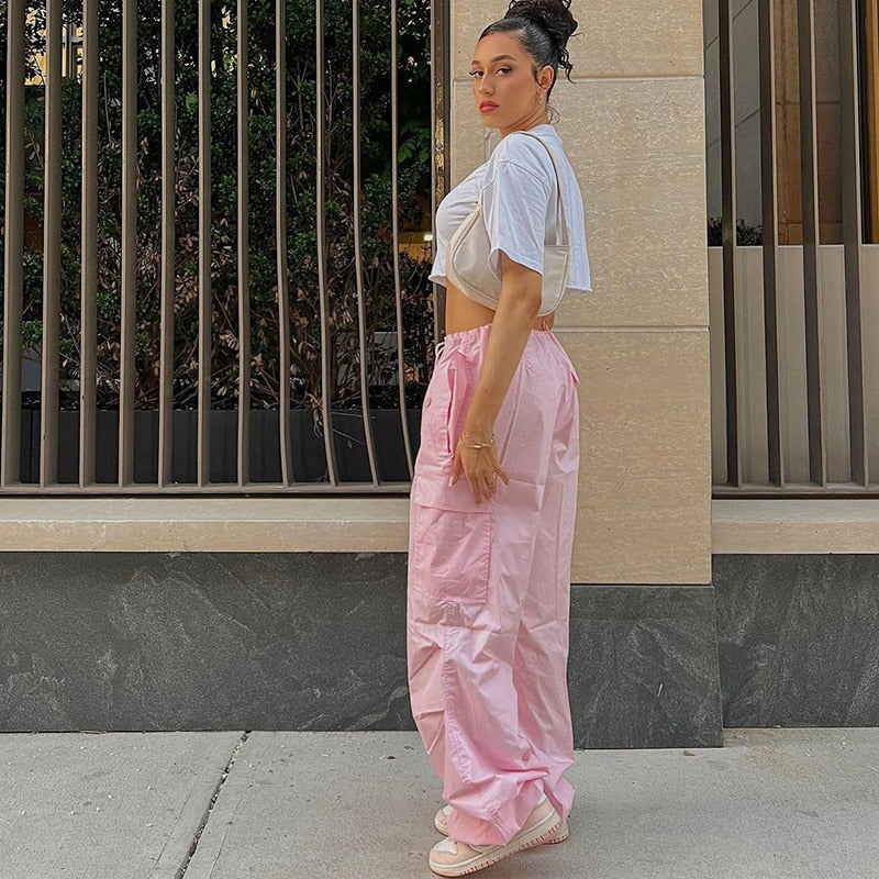 Frau in rosa Jogginghose und weißem Crop-Top, lässiger Streetstyle, städtische Kulisse.