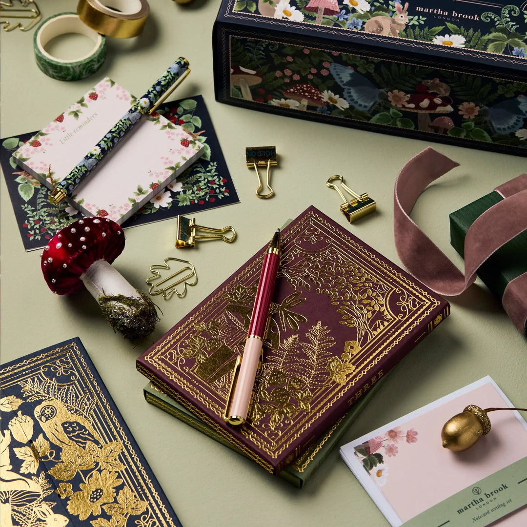 Luxus-Notizbuch mit goldener Prägung, Stifte, Briefpapier und Dekoration auf grünem Hintergrund.