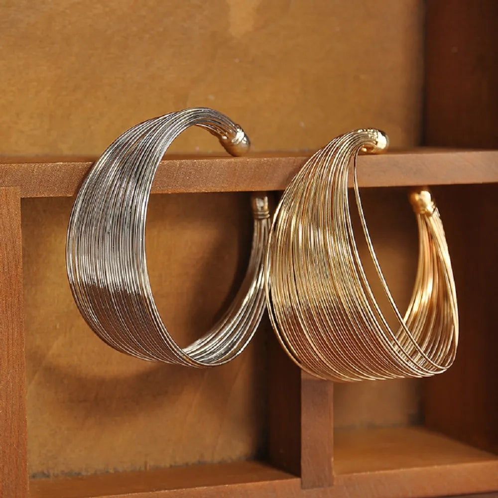 Zwei breite Armreifen aus Metall, silber und gold, auf Holzregal, modisches Schmuckdesign.