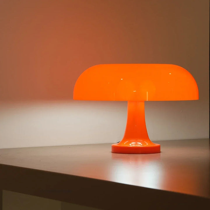 Boční pohled na oranžovou rozsvícenou lampu na hraně stolu, oranžové světlo se odráží na zdi a desce. 6