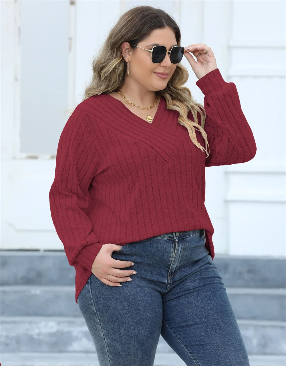 Frau in rotem Strickpullover, V-Ausschnitt, Sonnenbrille, blaue Jeans, lässige Mode.