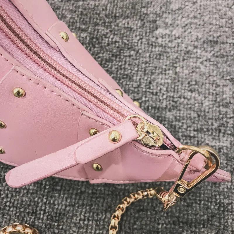 Rosa Lederhandtasche mit goldenen Nieten und Reißverschluss auf grauem Hintergrund.