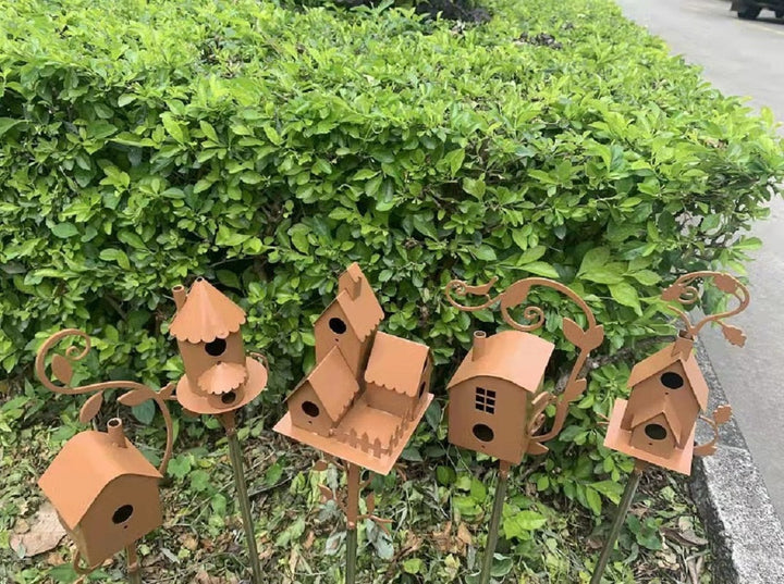 Rostfarbene Metall-Vogelhäuser im Garten, dekorative Gartenstecker, vor grüner Hecke.