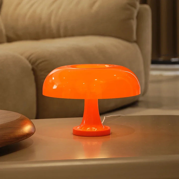 Lesklá oranžová lampa se svítící stopkou a bílým kabelem stojí na stolku před béžovou pohovkou. 5