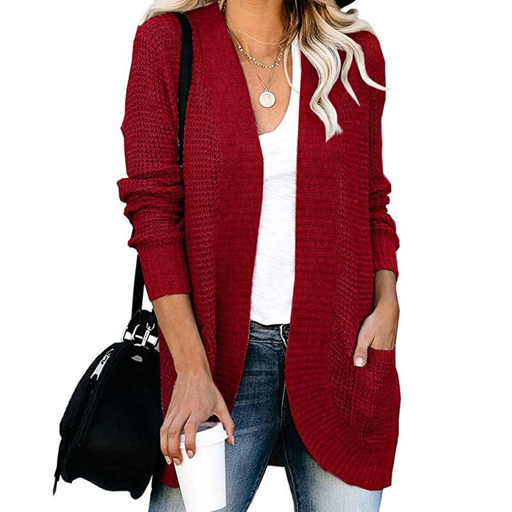 Frau in rotem Strickcardigan, weißem T-Shirt, Jeans, mit schwarzer Tasche und Kaffeebecher.