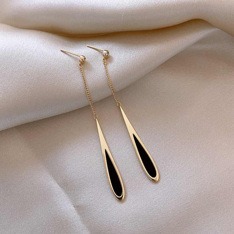 Goldene Ohrringe mit schwarzem Tropfendesign auf weißem Satin-Hintergrund.
