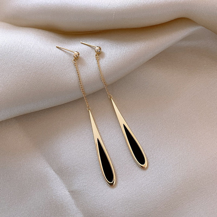 Goldene Ohrringe mit schwarzem Tropfendesign auf weißem Satin-Hintergrund.