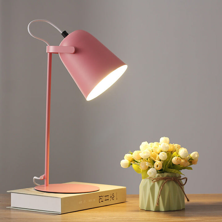 Růžová varianta lampy se svítícím stínidlem stojí na knize vedle kytice poupat v zeleném květináči. 8