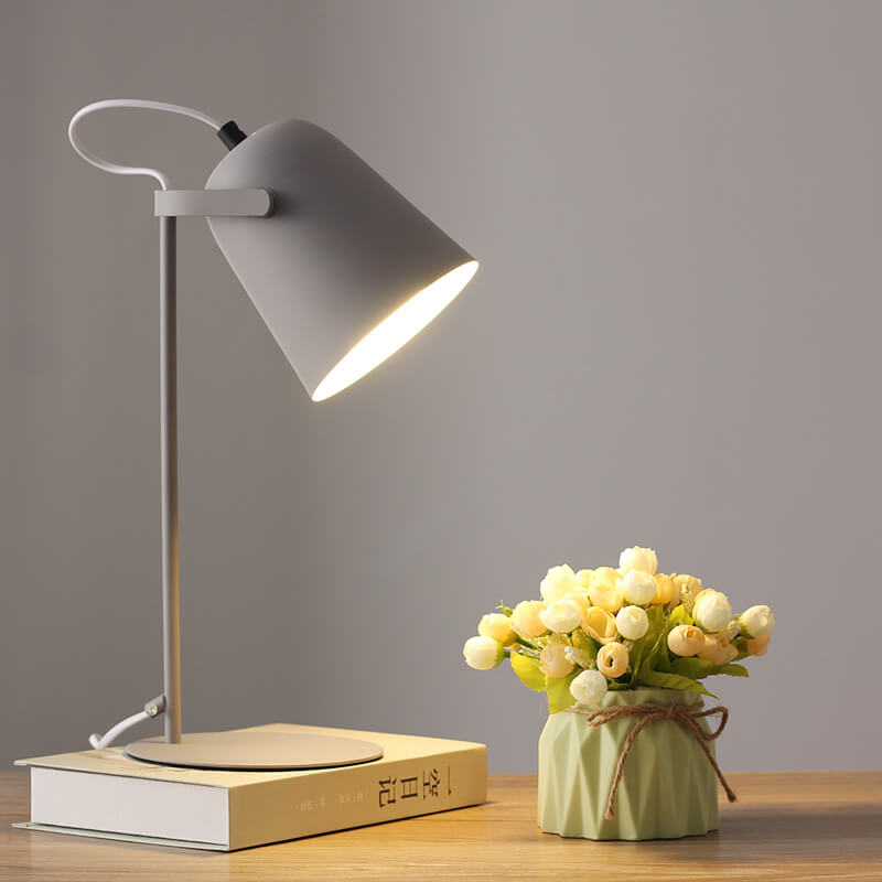 Šedá varianta lampy se svítícím stínidlem stojí na knize vedle kytice poupat v zeleném květináči. 10