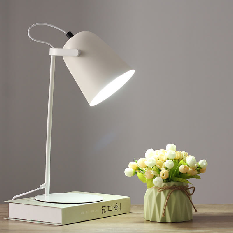 Bílá varianta lampy se svítícím stínidlem stojí na knize vedle kytice poupat v zeleném květináči. 11