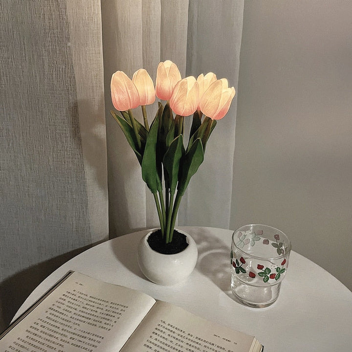 Künstliche Tulpenlampe in Vase auf Tisch neben Buch und Glas, warmes Licht, Dekoration.