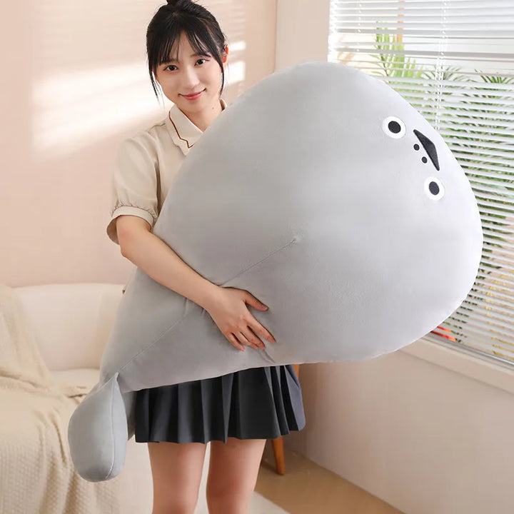 Frau hält großes graues Plüschtier in Form eines Fisches, gemütliches Kuscheltier, Geschenkidee.
