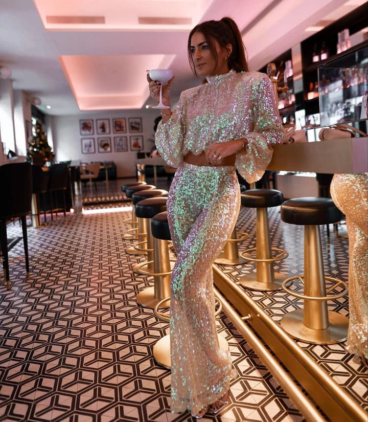 Frau in schimmerndem Paillettenanzug, hält Cocktail in moderner Bar, glamouröse Abendmode.