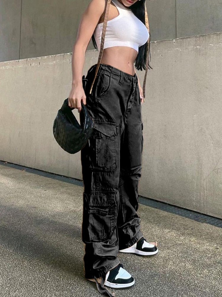 Frau in schwarzer Cargohose, weißem Crop-Top, Sneaker, modisch, urbaner Stil.