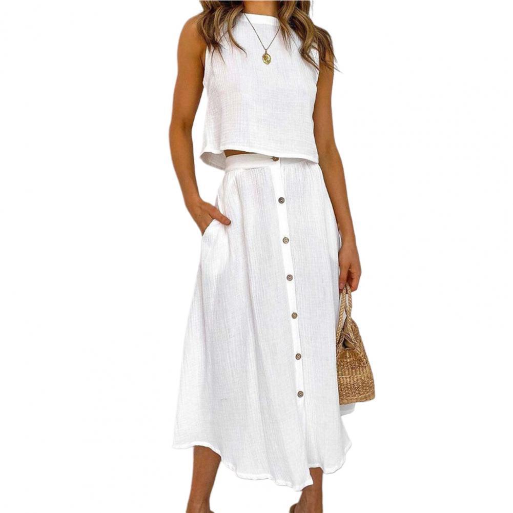Frau in weißem Leinen-Zweiteiler, ärmelloses Top, Knopfleiste, Sommermode, Strohtasche.