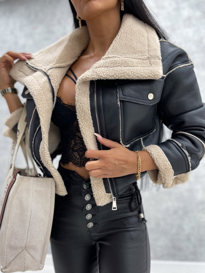 Frau in schwarzer Lederjacke mit Lammfellkragen, schwarze Spitzenbluse, weiße Tasche.